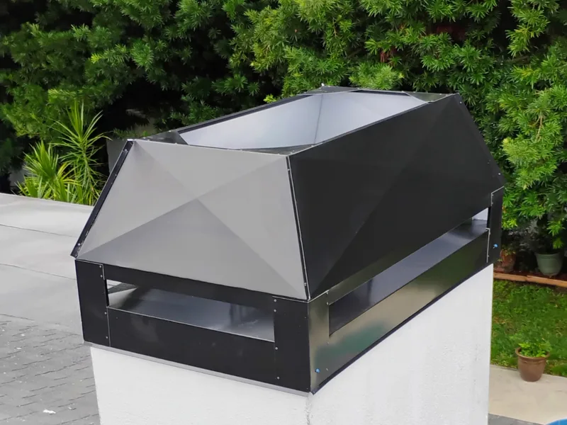 Black metal chimney cap mounted on stucco chimney with geometric faceted design