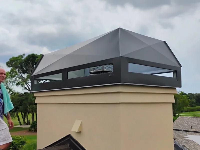 Black metal chimney cap with mesh screen on stucco chimney exterior