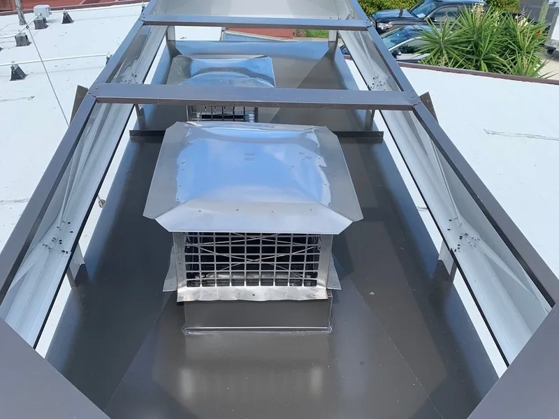Stainless steel chimney cap with mesh spark guard on flat metal roof