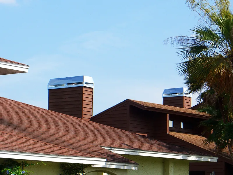 Stainless steel chimney caps on brown wood-clad chimneys above tile roof