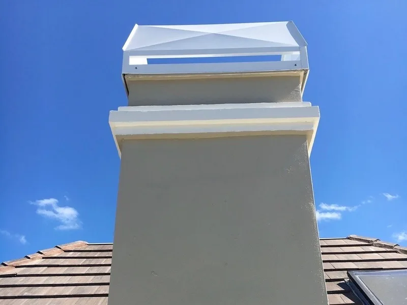 Stucco chimney with white metal cap against clear blue sky