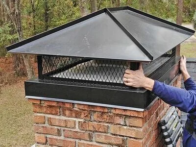 Black metal chimney cap installed on brick chimney by technician in FL