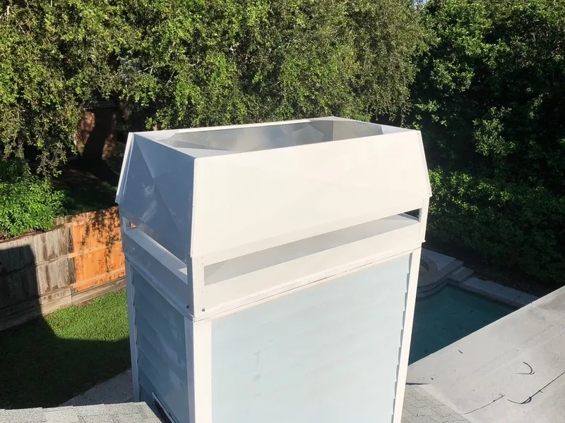 White metal chimney cap installed on flat roof stucco chimney